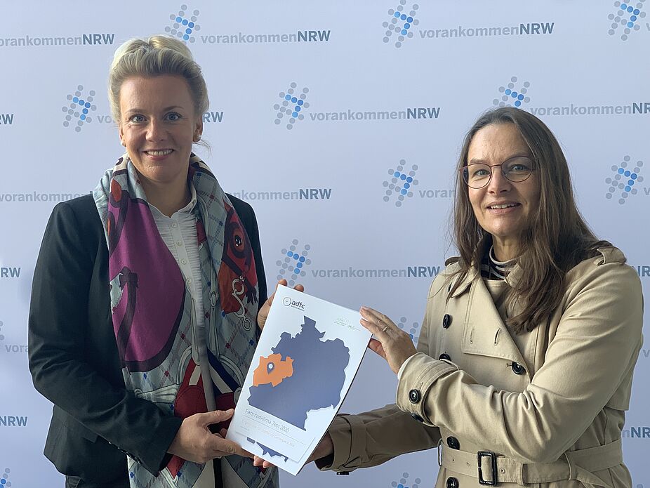 Isabelle Klarenaar vom ADFC NRW übergibt den ersten Fahrradklima-Test-Reader an Verkehrsministerin Ina Brandes.