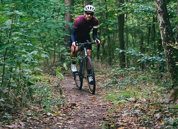 Ein Gravelbiker fährt auf einem schmalen Waldpfad.